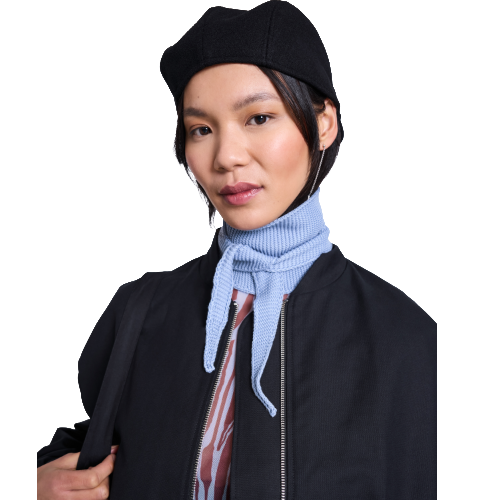 Woman wearing a black beret, black jacket, light blue knit scarf, and patterned top, looking at the camera with a neutral expression against a white background.