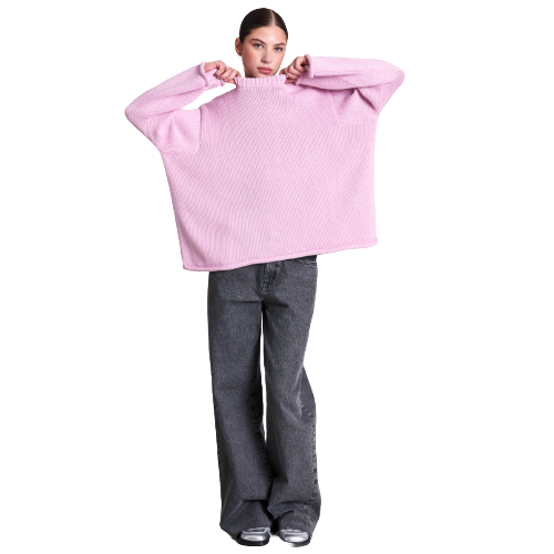 A person wearing an oversized pink sweater and wide-leg gray jeans stands with arms raised, holding the sweater’s collar, against a white background.