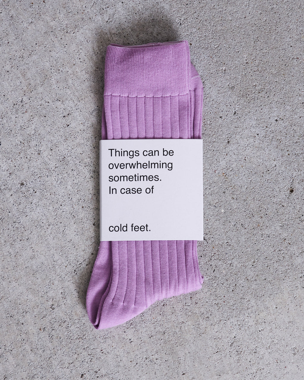 A pair of comfy, soft SOCKS ORCHID by jan-n-june in lavender organic cotton lies on a gray surface. A white card on top reads: Things can be overwhelming sometimes. In case of cold feet.