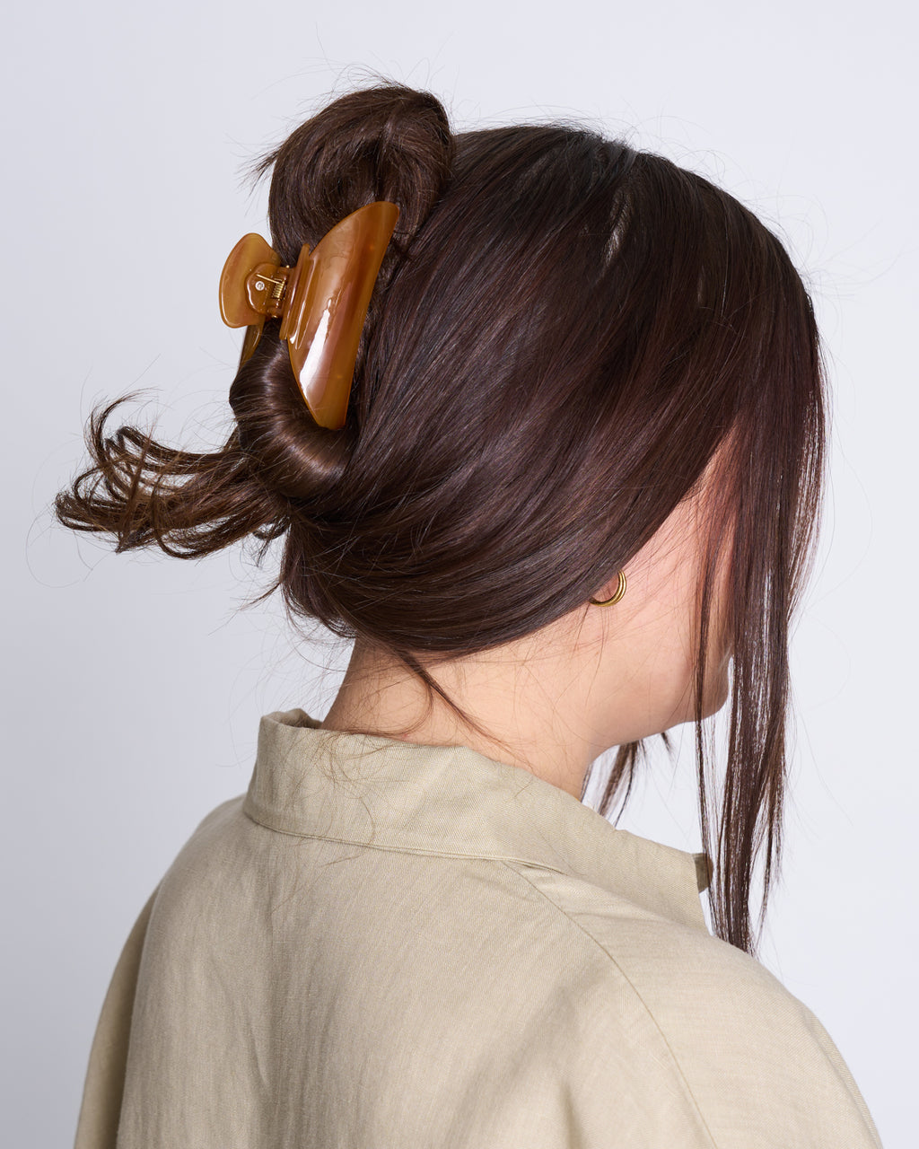 A person with long brown hair in a twisted updo, secured by the jan-n-june MIDI HEIRLOOM CLAW COGNAC, wears a beige collared shirt and faces away from the camera against a plain light background.