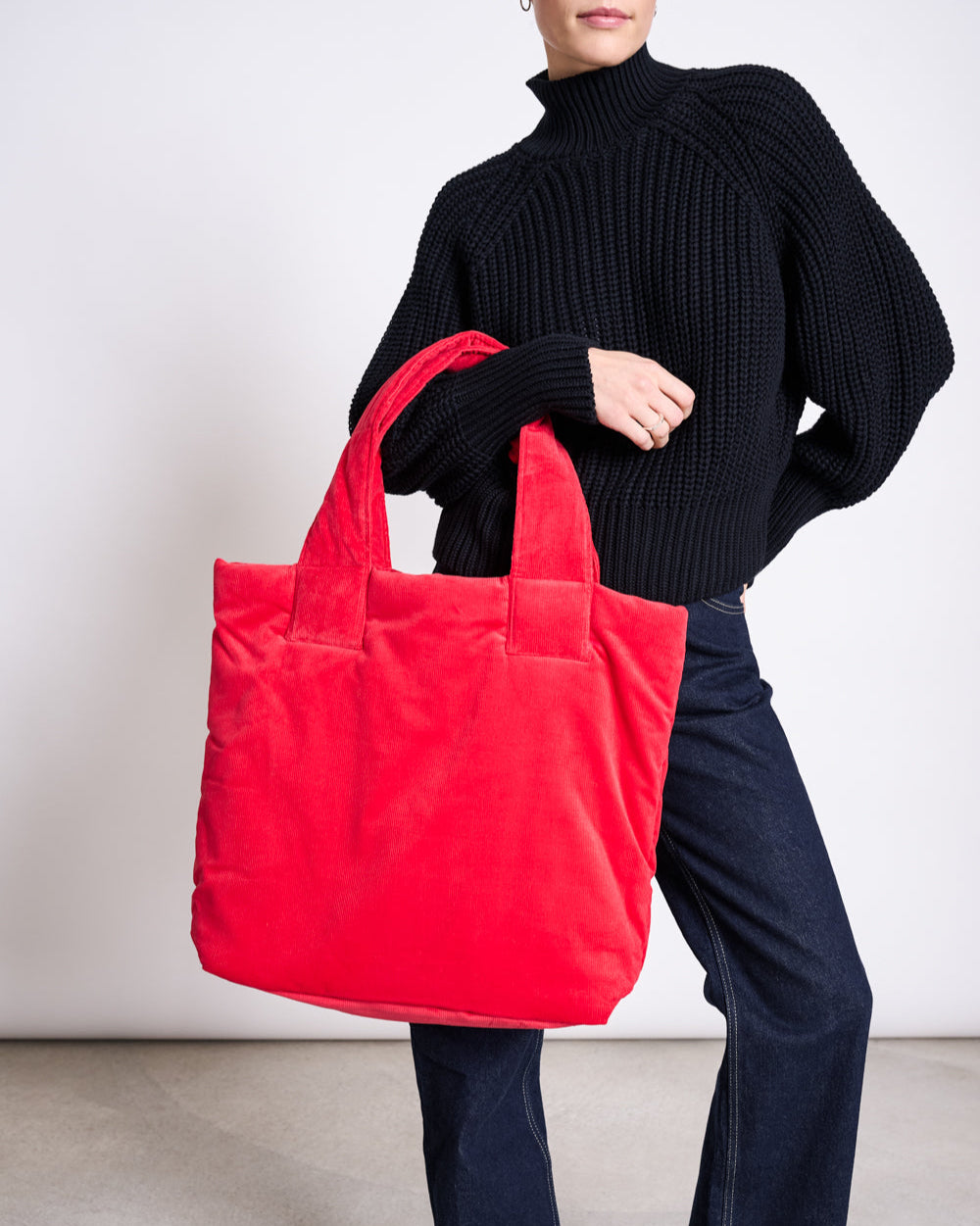 A person in a black sweater and dark jeans holds the jan-n-june PADDED SHOPPER SMOL RED with both hands against a plain background.