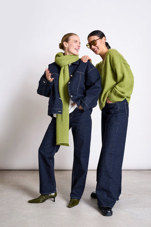 Two girls dressed in dark denim and green knitwear are laughing together.