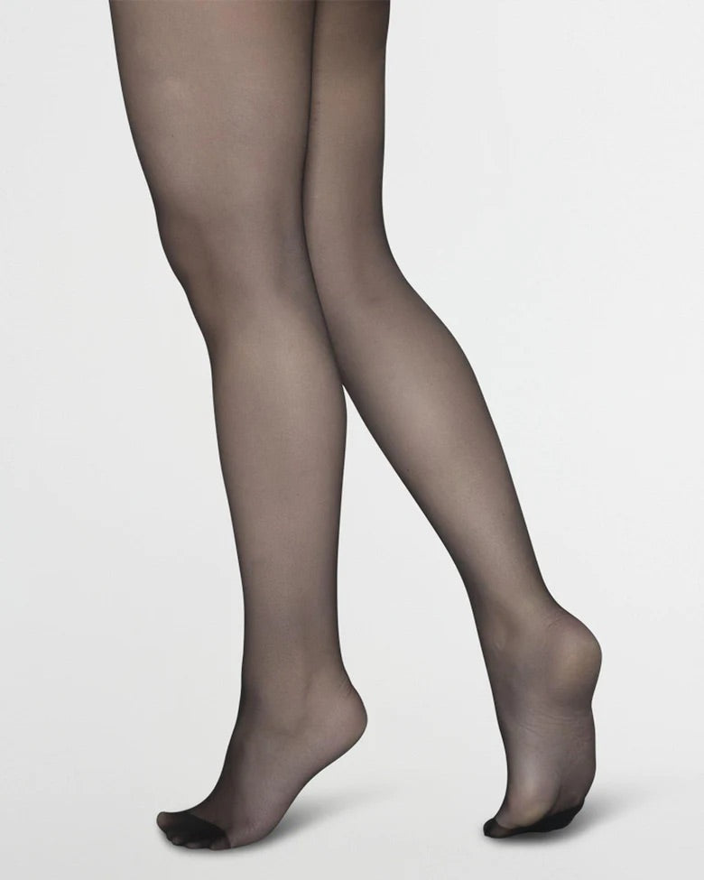 A person wearing jan-n-june SWEDISH STOCKINGS ELIN PREMIUM TIGHTS 2-PACK BLACK, made in Italy, stands with one leg slightly bent behind the other against a plain light background.
