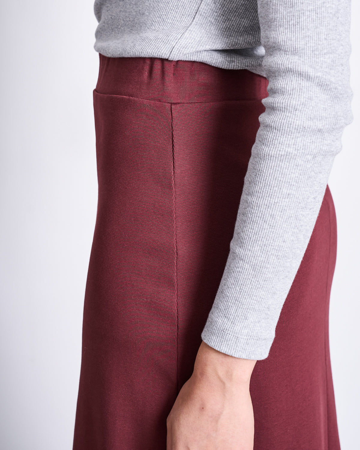 A side view shows a person in a light gray long-sleeve top and the jan-n-june MAXI SKIRT BURNITA INTENSE RUST GOTS, highlighting the waist and arm.