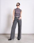 A woman in jan-n-june’s RUFFLE TOP LAGUNA LEO PRINT, black sunglasses, high-waisted wide-leg gray jeans, and black heeled boots stands on a concrete floor against a plain white background.