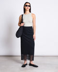 A woman wearing sunglasses, the jan-n-june LYOCELL RIB TANK TOP PORTO VINTAGE LACE, a long black skirt, black flat shoes, and a black shoulder bag stands against a white background.