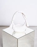 The jan-n-june BAG BIWA PUFFY MICRO ICE, a white crescent-shaped ultralight bag with knotted handles, is displayed on a mirrored cube against a simple, light backdrop.