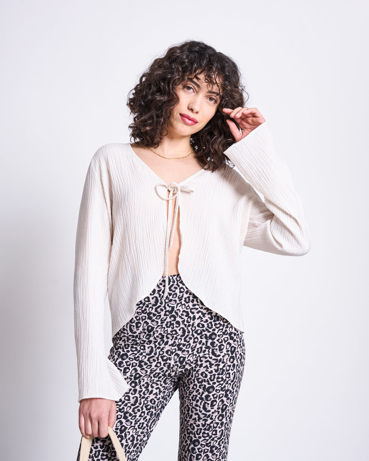 A woman with curly hair models jan-n-junes LEGGINGS LEO GOTS, featuring a black-and-white leo print, paired with a cream long-sleeve top and a small light-colored bag against a plain white background.