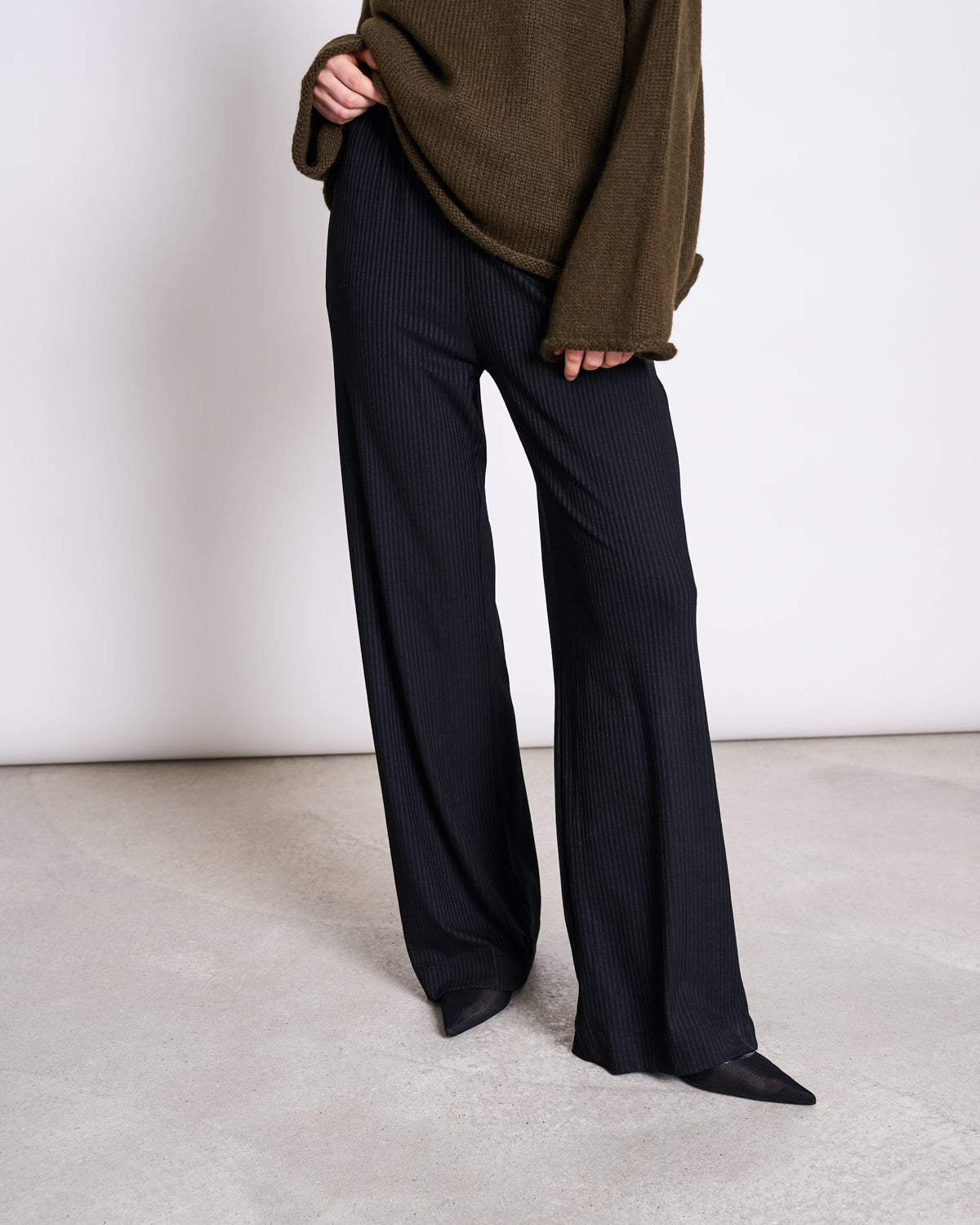 A person wears loose black pinstripe pants, black pointed-toe shoes, and the jan-n-june OVERSIZED ALPACA MIX JUMPER WOOLY SONA ROSEMARY, standing on a light floor with a plain background.