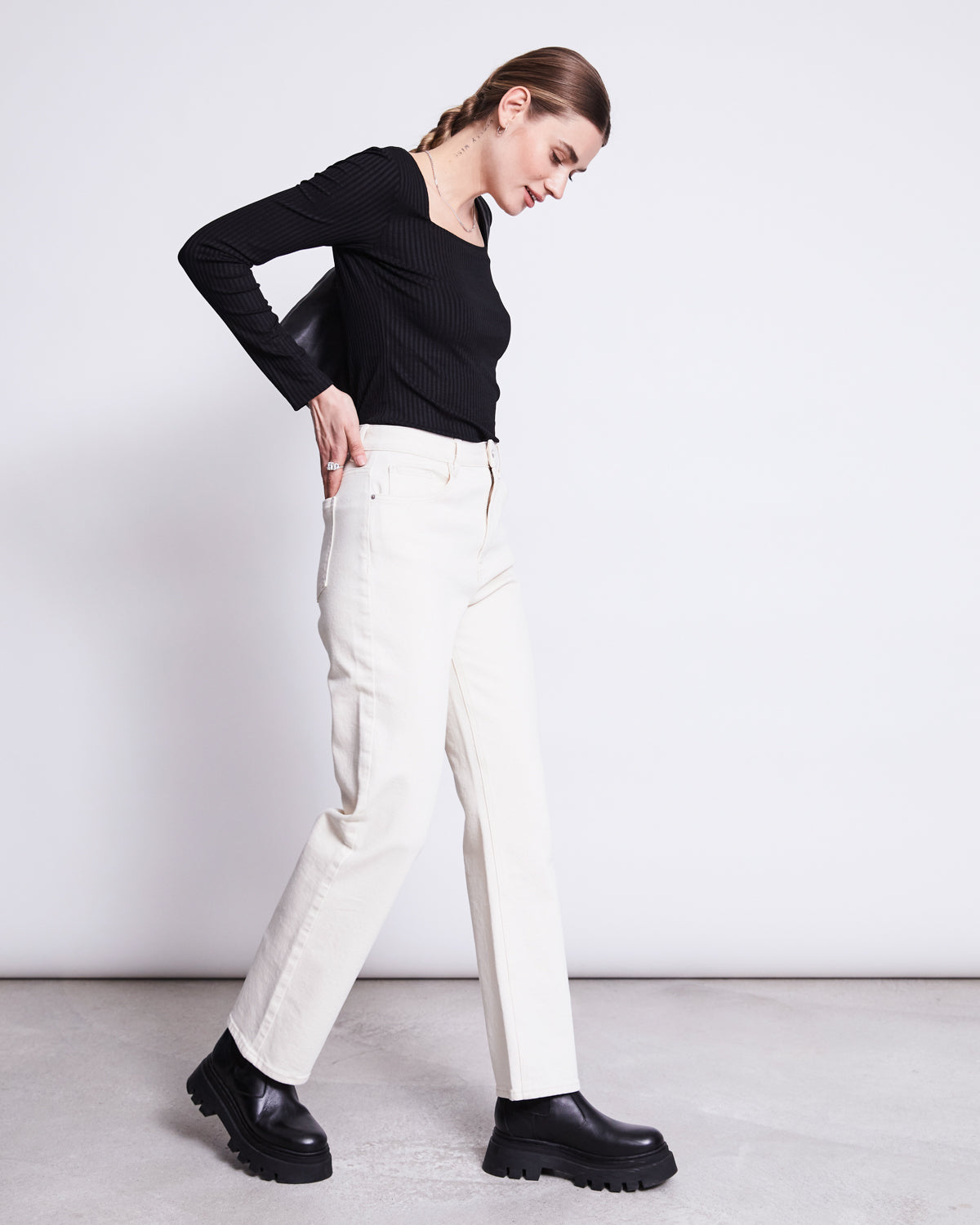 A woman with braided hair wears the jan-n-june SQUARE NECK LONGSLEEVE FRIA BLACK, paired with off-white straight-leg jeans and black chunky boots, walking against a plain light background.