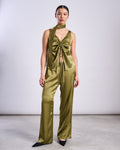 A person stands against a plain backdrop wearing an elegant olive green vegan silk sleeveless top, matching wide-leg pants, and the jan-n-june SILKY SCARF PIURA WOODY OLIVE draped around their neck with black pointed shoes.