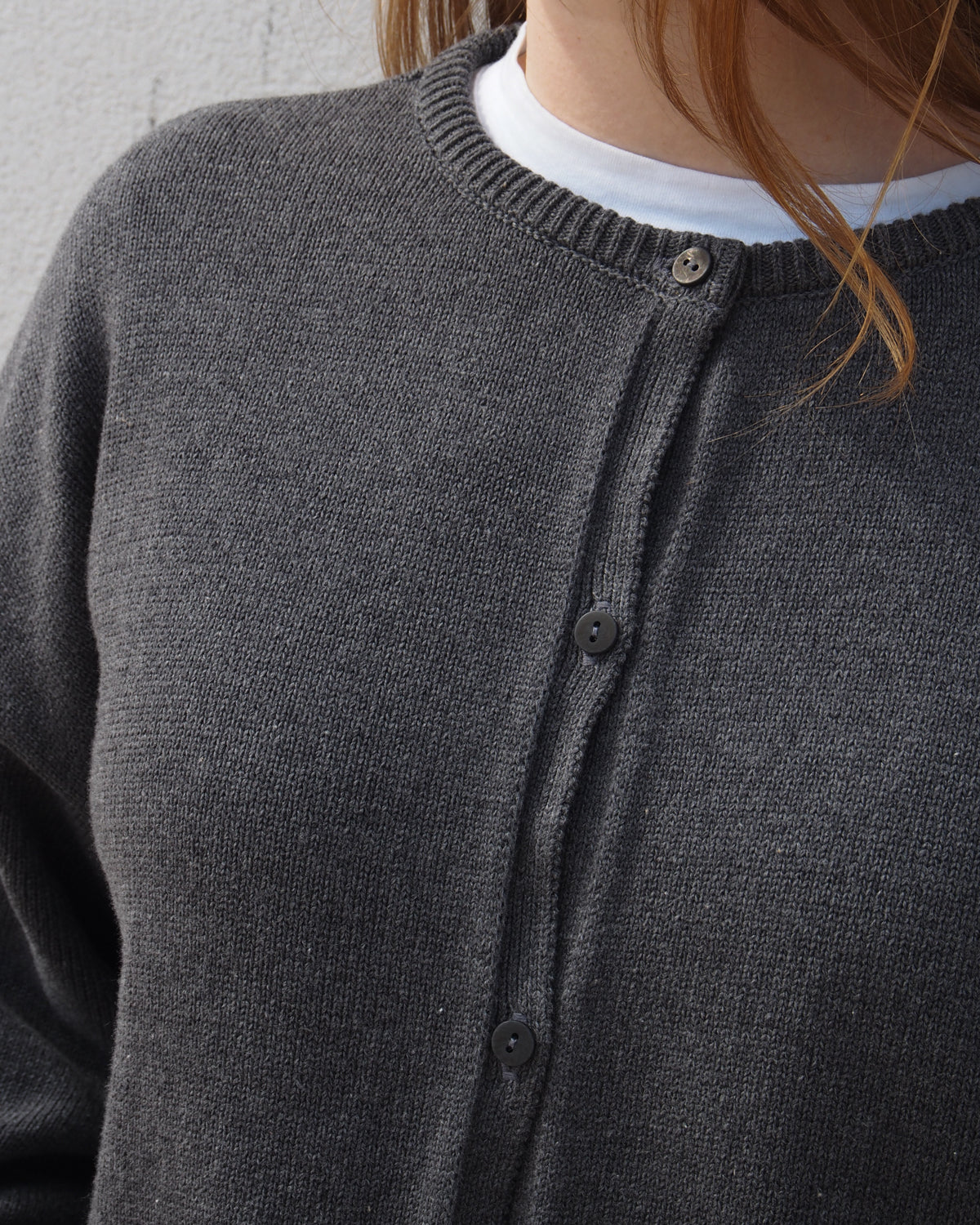 A person wears the jan-n-june LIGHT CARDIGAN ASAS DARK GREY GOTS over a white organic cotton T-shirt. The cropped image, highlighting the chest and neck, hints at sustainable fashion.