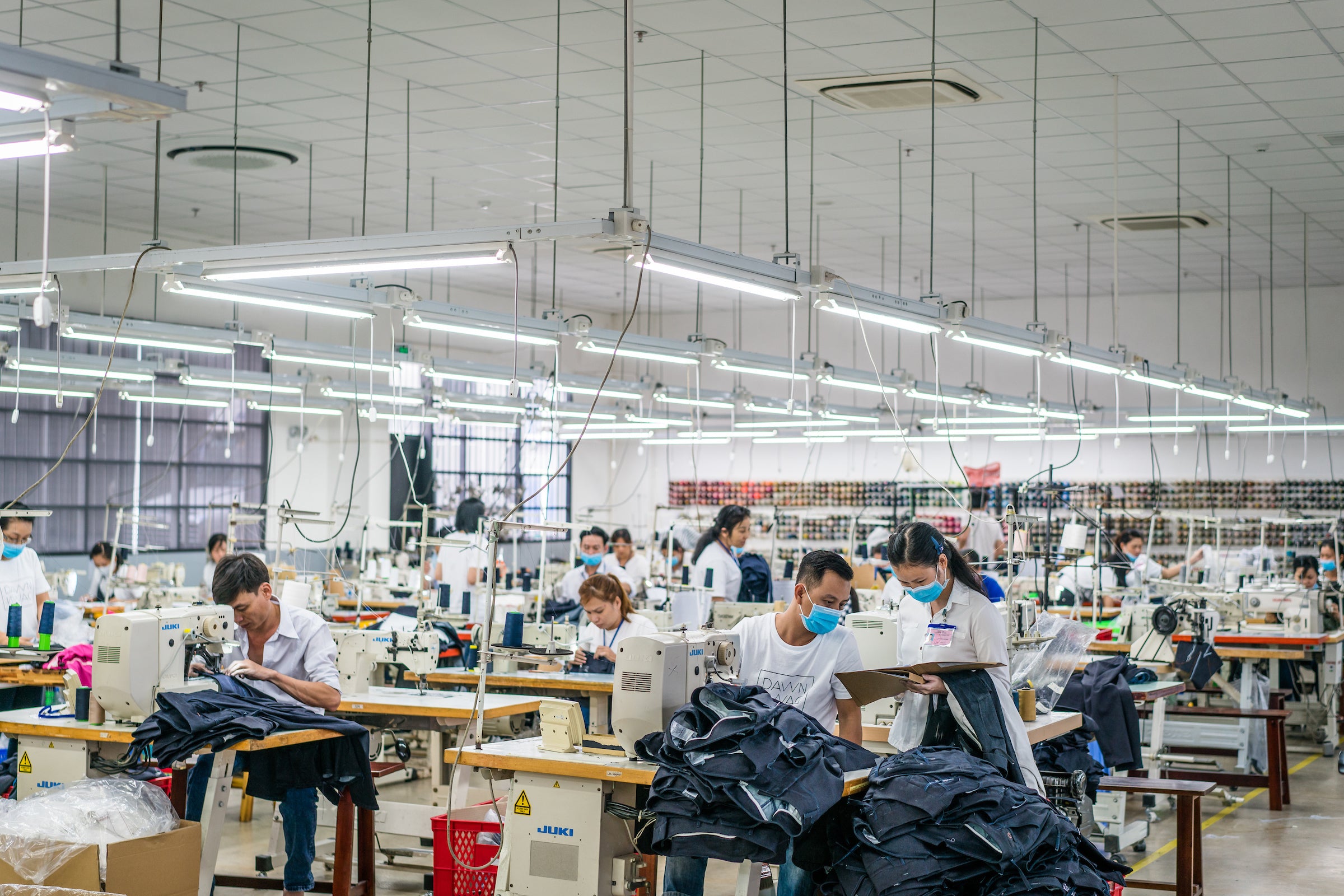 Denim factory with several people dressed in white t-shirts sewing jeans.