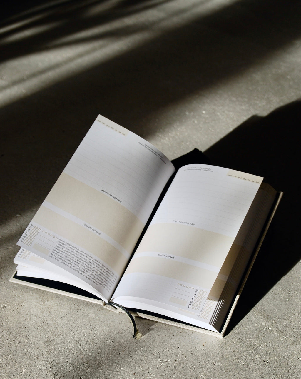 The jan-n-june DIARY A GOOD DAY NATUR rests on a sunlit concrete surface, its blank pages inviting mindfulness and self-reflection. Light and shadows create a calm, minimalist mood.