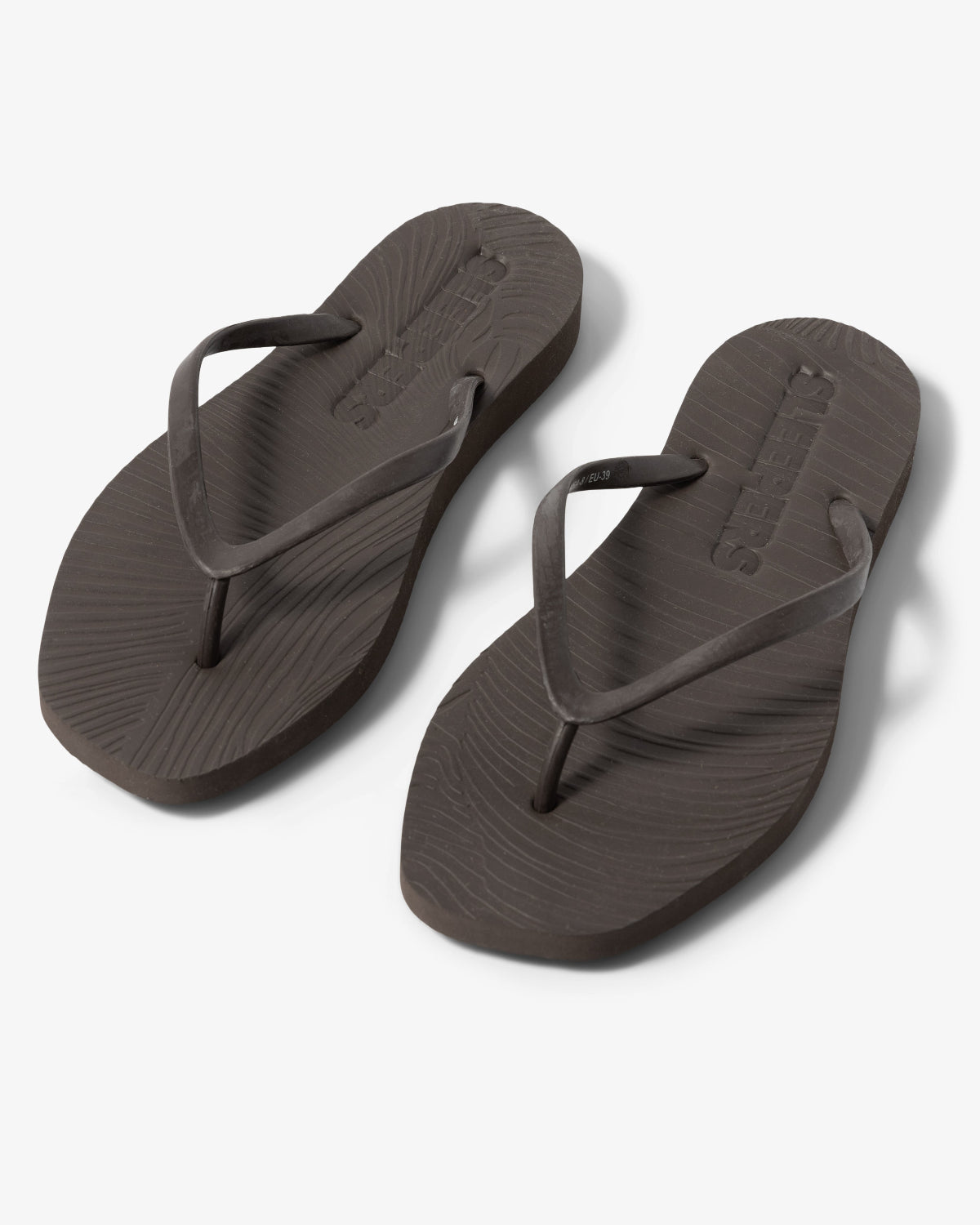 The jan-n-june SLEEPERS TAPERED FLIP FLOPS BROWN are dark brown, biodegradable flip-flops with textured footbeds and simple thong straps, shown on a light gray background.