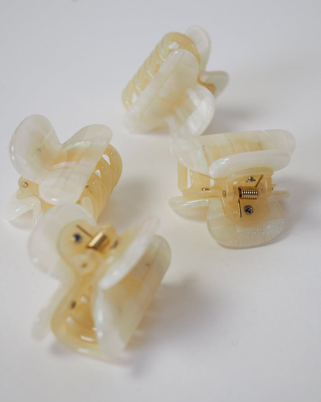 Four MINI HEIRLOOM CLIP OPALITE SHELL CHECKER hair claws by jan-n-june, handcrafted in Italy from sustainable acetate, feature a pearly cream checker pattern with gold springs and glossy marbled finish, arranged stylishly on a white surface.