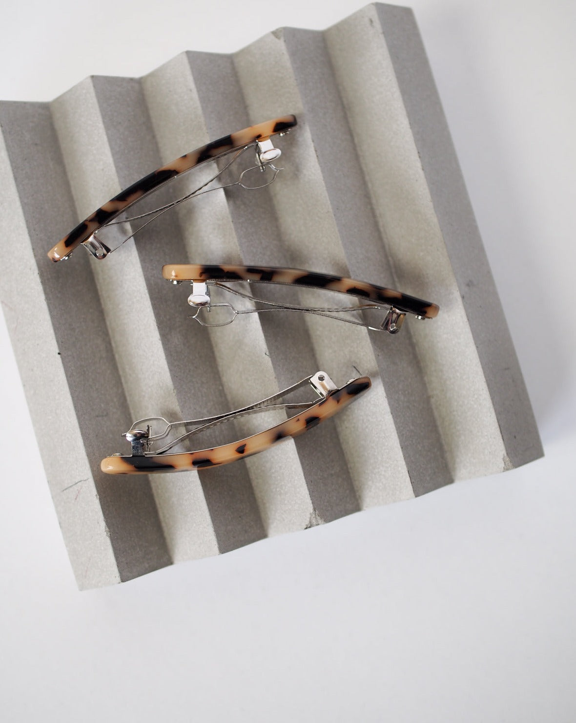 Three JAN N JUNE MIDI PARIS BARRETTE BLONDE TORTOISE hair clips with metal clasps are arranged diagonally on a wavy gray surface.