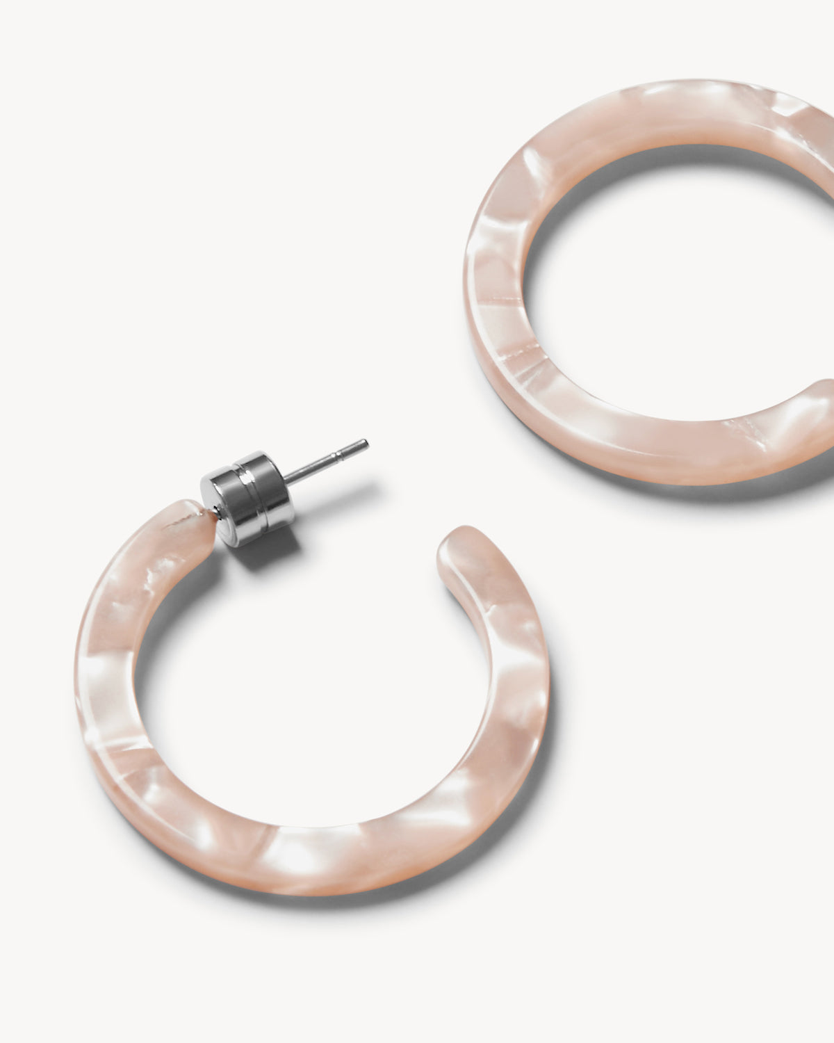 The MINI HOOPS PEACH SHELL by jan-n-june are round, open acetate mini hoop earrings with a marbled, pearly pink finish and silver-tone posts, shown against a plain white background.