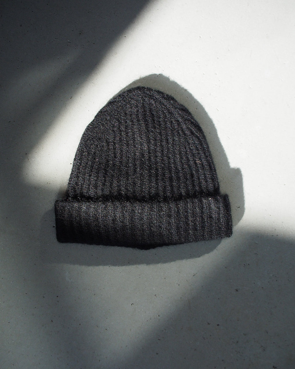 The jan-n-june WOOLY KNIT BEANIE BJON BLACK, made from mohair and wool, rests on a light gray surface with partial shadows in the background.