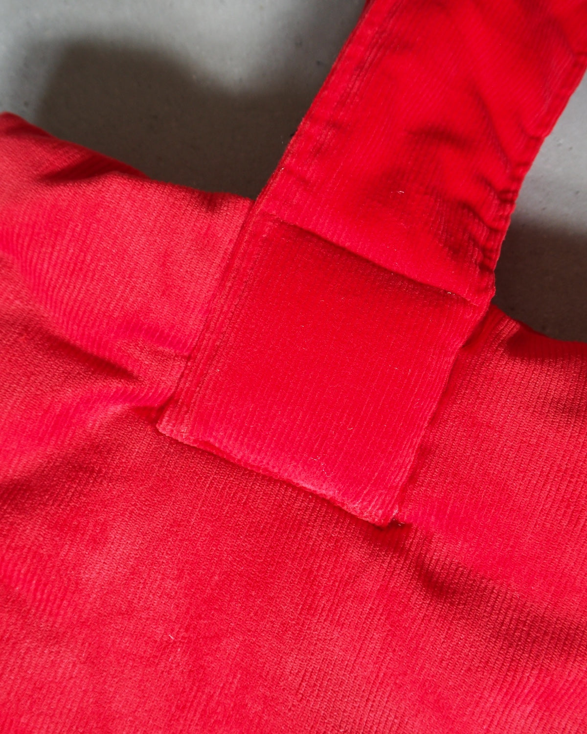 Close-up of the jan-n-june PADDED SHOPPER SMOL RED, made from deadstock fabric with a corduroy-like texture, thick handle, and visible stitching, set against a gray background.