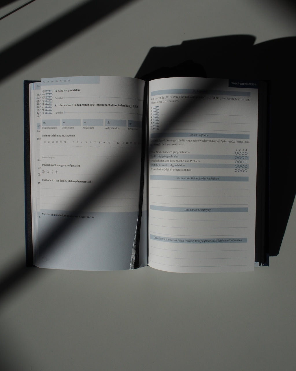 The TAGEBUCH EINE GUTE NACHT sleep diary by jan-n-june rests on a white surface in sunlight, showing pages with printed checkboxes, scales, and blank lines for mindful nightly reflections.