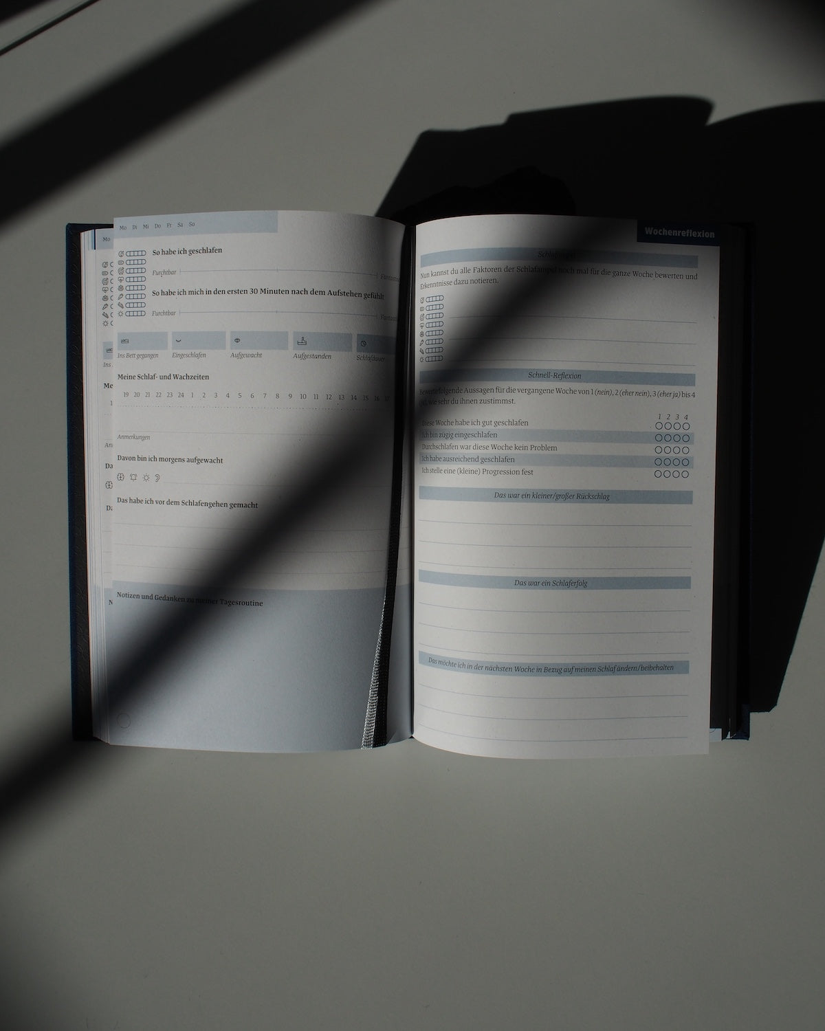 The TAGEBUCH EINE GUTE NACHT sleep diary by jan-n-june rests on a white surface in sunlight, showing pages with printed checkboxes, scales, and blank lines for mindful nightly reflections.