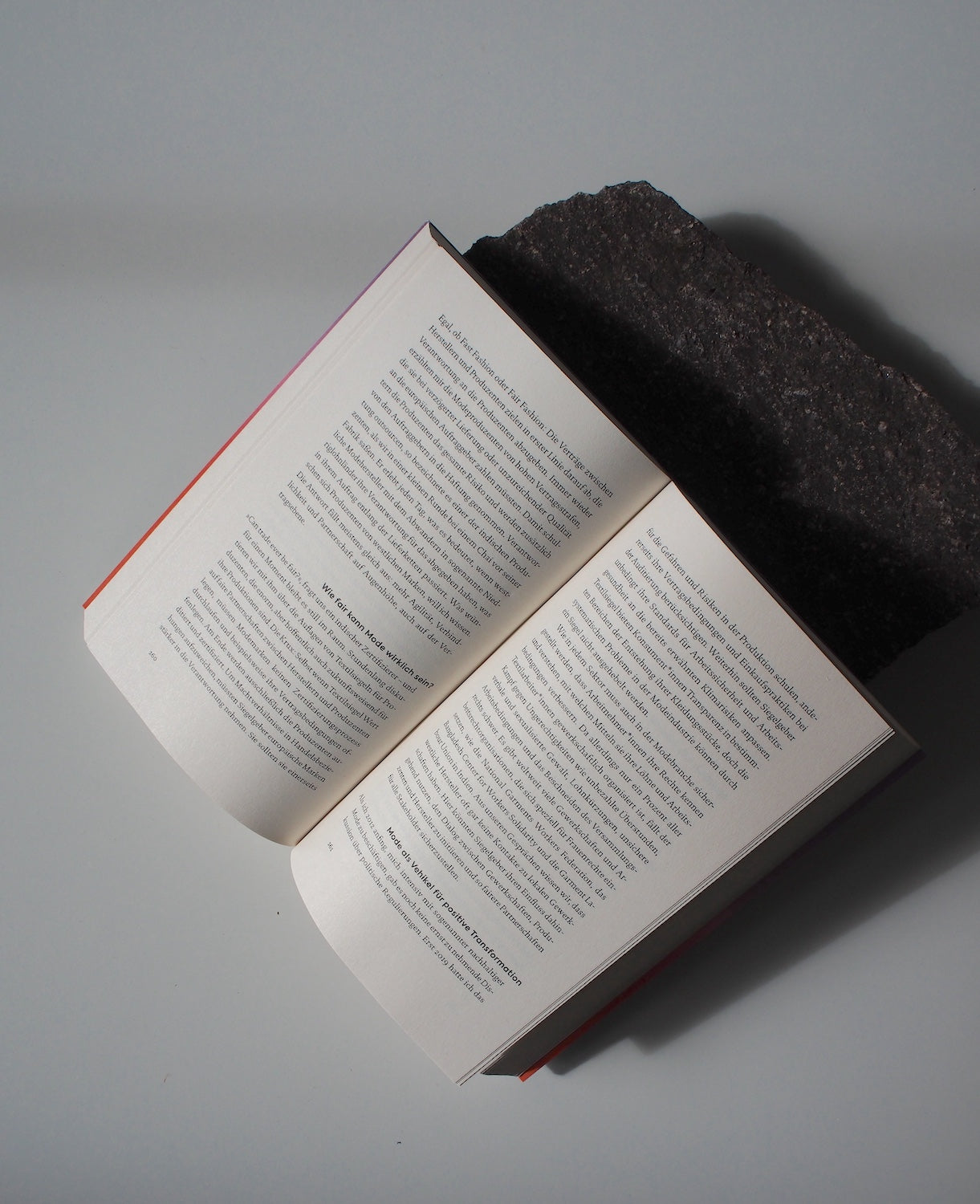 An open book lies flat on a light surface, its top edge against a dark stone. Shadows cross the text-filled pages, inviting thoughts of a climate-friendly future with jan-n-june’s UNLEARN CO2.
