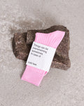 SOCKS BONBON PINK by jan-n-june: soft, organic cotton socks in pink with a label that reads, Things can be overwhelming sometimes. In case of cold feet. Displayed on a rough brown stone atop concrete.