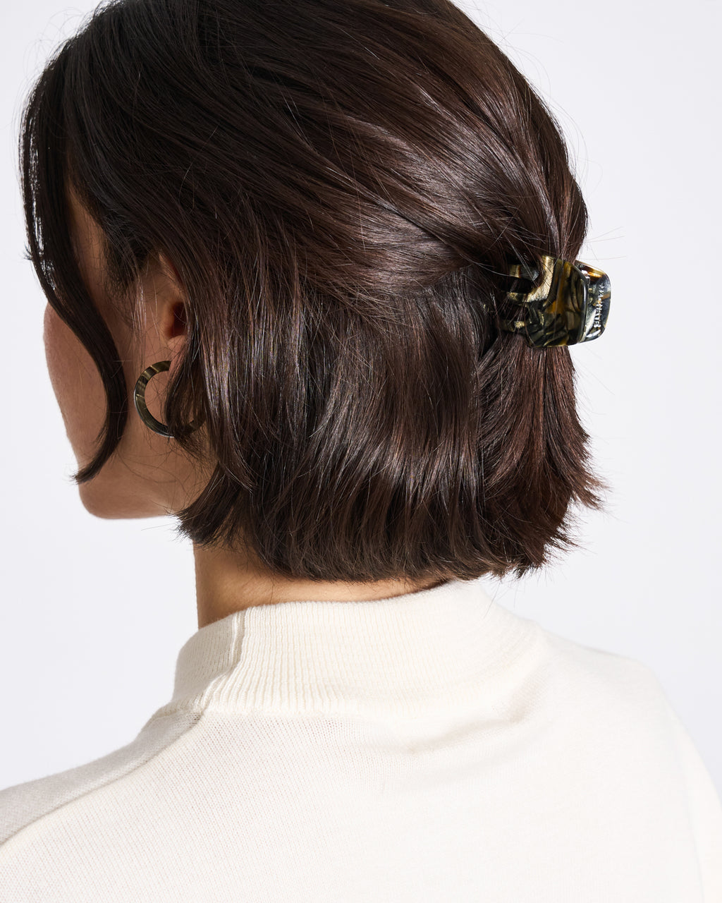 A person with short, dark brown hair clipped back with the jan-n-june MINI CLAW MIDNIGHT HORN—handcrafted in Italy—wears a white top and hoop earrings, shown from the back and slightly to the side.