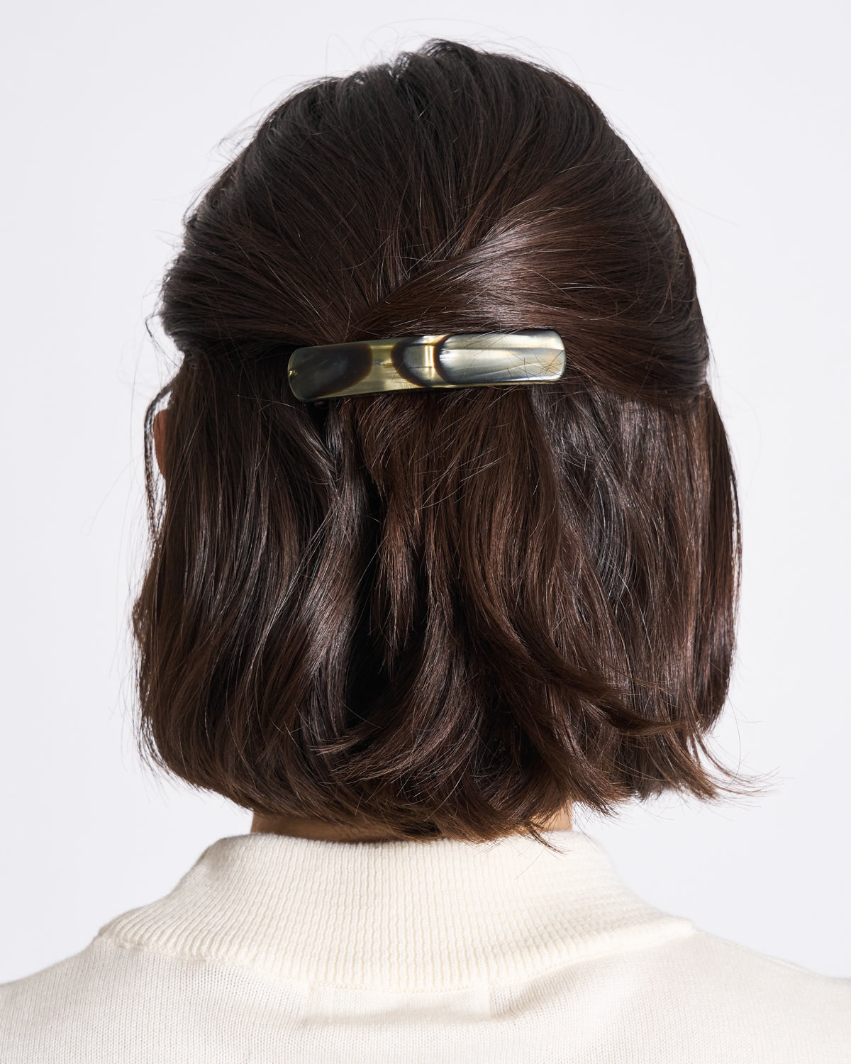 A person with short, dark brown hair, styled from behind with the jan-n-june HEIRLOOM BARRETTE MIDNIGHT HORN, captures effortless French chic alongside a cream-colored top.