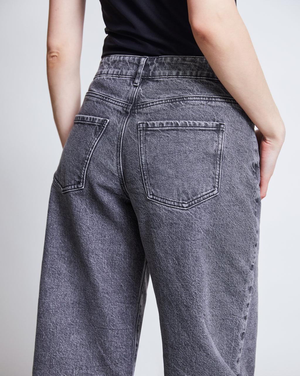 A person is shown from the back wearing jan-n-june WIDE LEG JEANS SUNNY LIGHT GREY with a black top, highlighting the sustainable jeans high-waisted fit, faded gray tone, and detailed back pockets and seams.