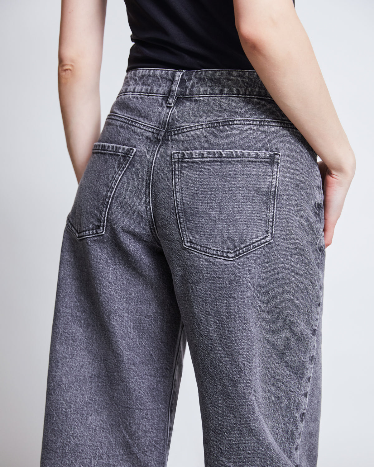 A person is shown from the back wearing jan-n-june WIDE LEG JEANS SUNNY LIGHT GREY with a black top, highlighting the sustainable jeans high-waisted fit, faded gray tone, and detailed back pockets and seams.