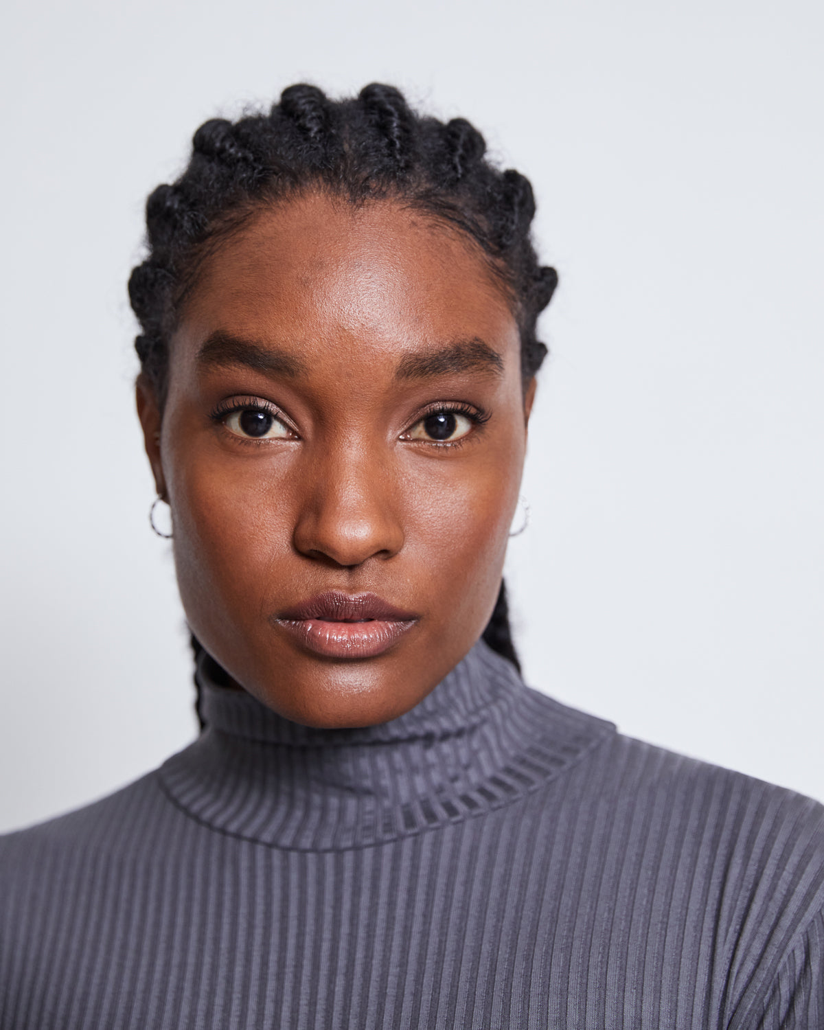 A woman with braided hair and small hoop earrings wears the jan-n-june LYOCELL TURTLENECK MIO DARK GREY, looking directly at the camera with a neutral expression against a plain light background.