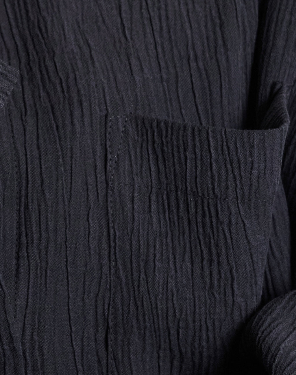 Close-up of the jan-n-june CRINKLE SHIRT SKUR BLACK, featuring a textured, wrinkled surface and visible pocket. Made from soft Tencel™ Lyocell, its raised lines and tactile finish are highlighted in the lighting.