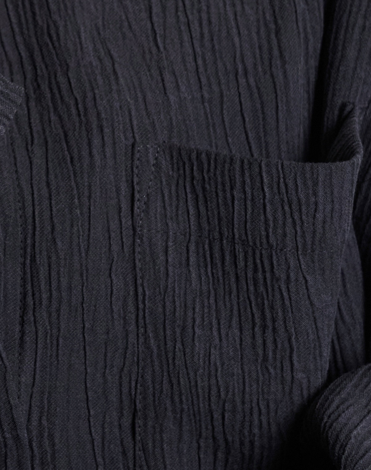Close-up of the jan-n-june CRINKLE SHIRT SKUR BLACK, featuring a textured, wrinkled surface and visible pocket. Made from soft Tencel™ Lyocell, its raised lines and tactile finish are highlighted in the lighting.