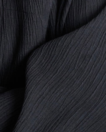 Close-up of jan-n-june’s CRINKLE PANTS HAVA BLACK, crafted from black Tencel™ Lyocell fabric with a crinkled texture and fine vertical lines, creating a wavy pattern for a stylish look.