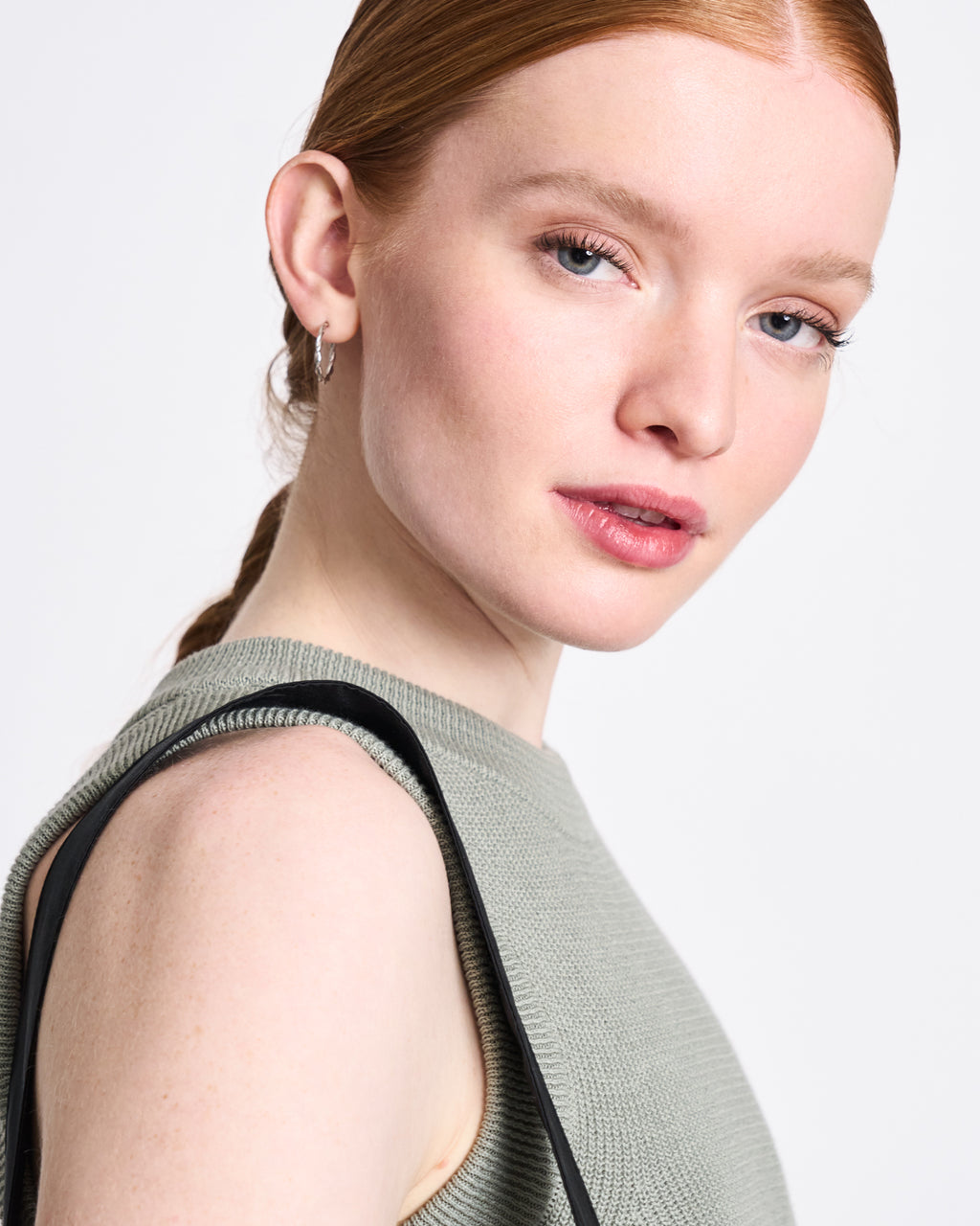 A woman with fair skin and straight red hair wears the jan-n-june KNIT TOP GARDA MUTED SEA SPRAY GOTS and a small hoop earring, looking toward the camera against a plain white background.