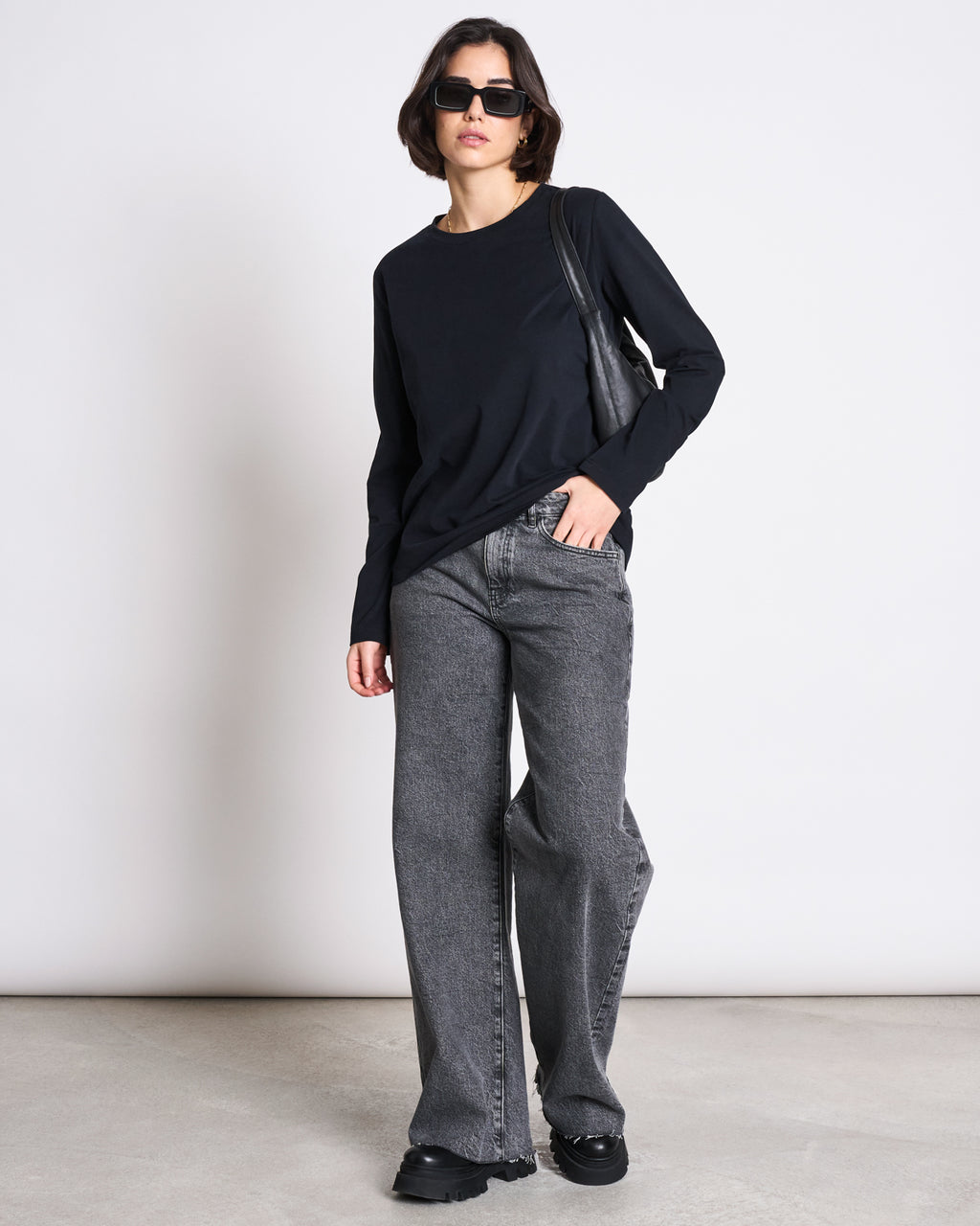 A person wearing the jan-n-june BRUSHED LONGSLEEVE BOY BLACK GOTS pairs it with gray wide-leg jeans, black shoes, sunglasses, and a black bag while standing against a plain white background.