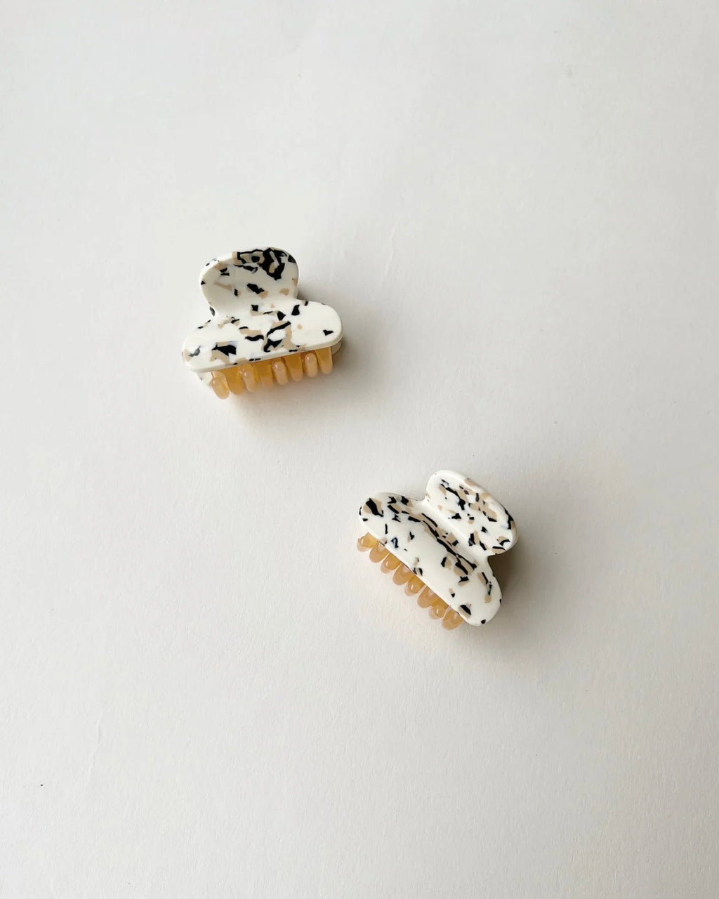 Two MINI HEIRLOOM CLIP TERRAZZO hair claws by jan-n-june, in white acetate with black speckles, rest on a neutral background, adding a touch of French chic style.