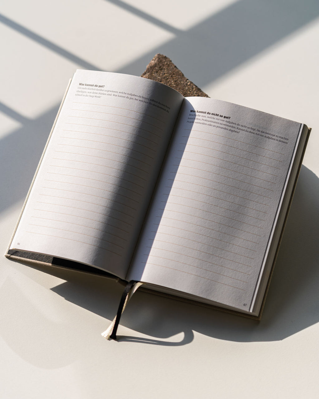 The jan-n-june PLANER EIN GUTES PROJEKT NATUR, an open mindful success journal with lined pages and a fabric bookmark, rests on a light surface with sunlight casting shadows—sustainably made in Germany for your holistic schedule.