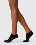 A person wears jan-n-june SWEDISH STOCKINGS SOCKS SARA BLACK, made from recycled yarn, standing on tiptoe with one leg slightly bent, against a plain light gray background.