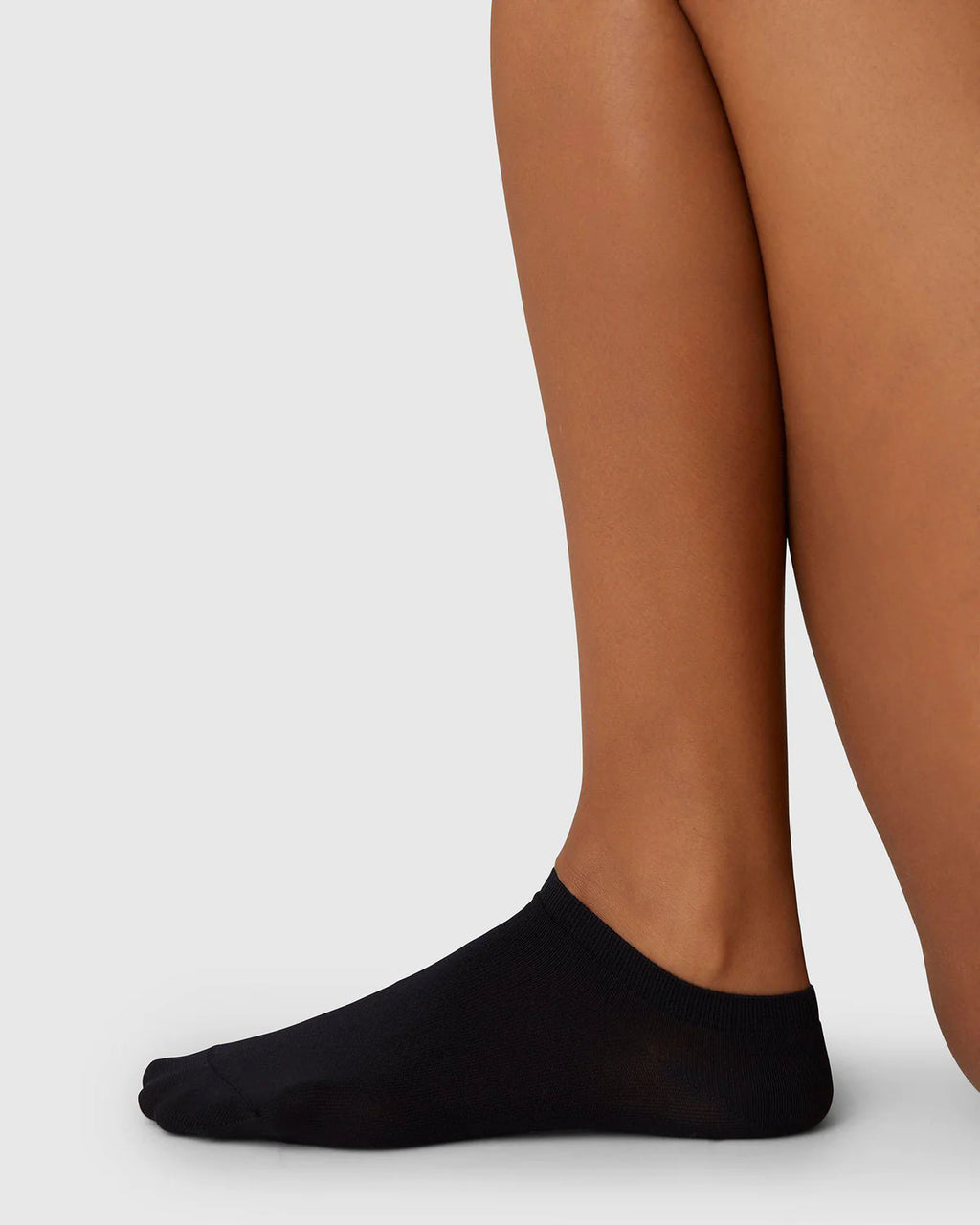 A close-up side view of a persons lower legs and feet wearing SWEDISH STOCKINGS SOCKS SARA BLACK by jan-n-june, made from recycled yarn, against a plain light gray background.