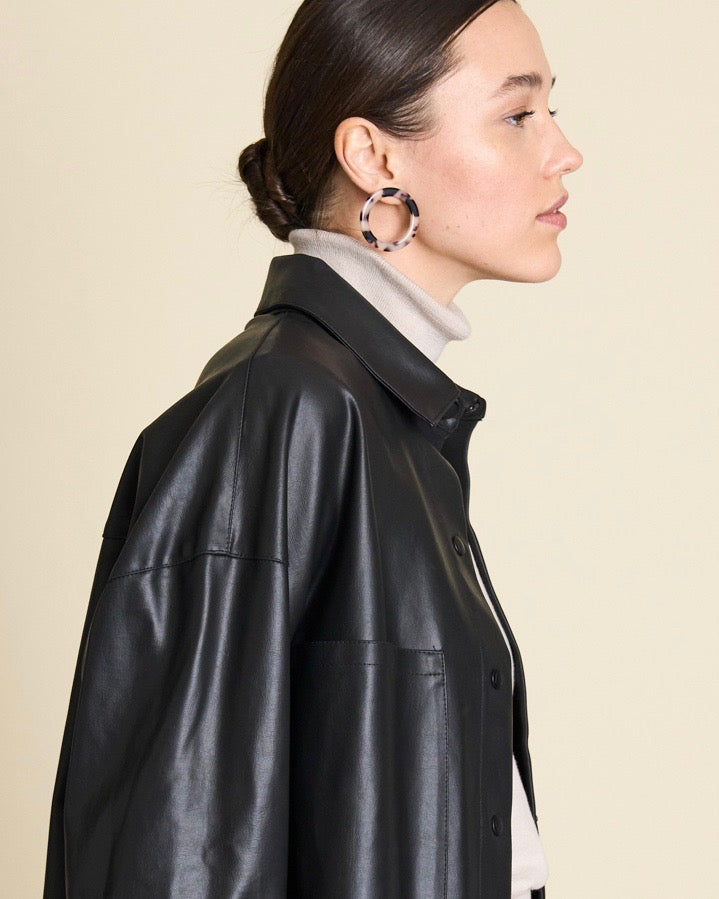 A woman with dark hair tied back wears a black leather jacket, light turtleneck, and large jan-n-june ISLA HOOPS ASH BLONDE TORTOISE, shown in profile against a plain beige background.