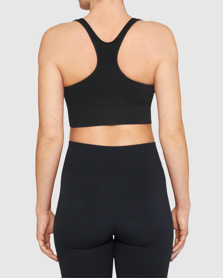 A person is shown from the back wearing the SWEDISH STOCKINGS WILMA SOFT BRA BLACK and high-waisted black leggings by jan-n-june, both made with recycled yarns, against a plain light gray background.