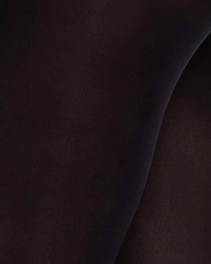 Close-up of jan-n-june SWEDISH STOCKINGS OLIVIA PREMIUM TIGHTS BLACK 60 DEN, semi opaque and smoothly stretched over legs, showcasing the recycled yarn fabric’s texture and fit.