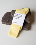 A pair of SOCKS FADED LEMON by jan-n-june rests on dark stones. Made from soft organic cotton, these yellow socks have a white label stating: Things can be overwhelming sometimes. In case of cold feet.