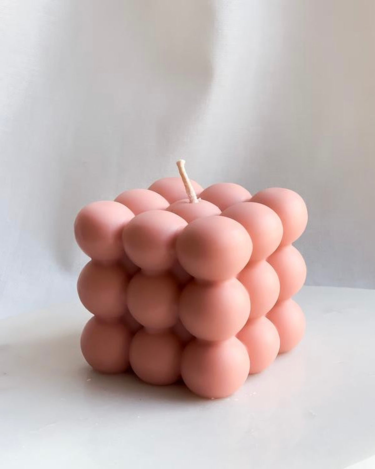 The BUBBLE TROUBLE CANDLE ROSE by jan-n-june is a pink, cube-shaped candle made of small round bubbles, displayed on a white surface against a plain light background.