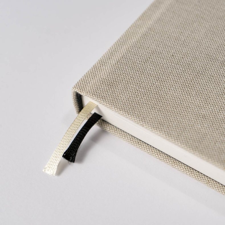 A close-up of the beige textured KALENDER EIN GUTER PLAN NATUR UNDATED hardcover diary by jan-n-june, with cream and black ribbon bookmarks on a white surface—ideal for mindful planning.